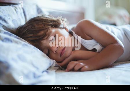 Ein kleines Kind schläft auf einem bequemen Bett, das in sanftes Morgenlicht getaucht ist. Ihr heiterer Ausdruck spiegelt tiefe Entspannung wider und zeigt Unschuld A Stockfoto