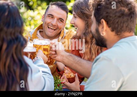 Nahaufnahme von Freunden, die mit Biergläsern im Garten tosten. Dynamische Momente, die Freundschaftsfeiern und soziale Bindungen während der Freizeit festhalten Stockfoto