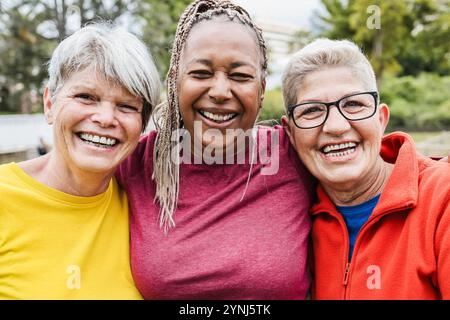 Glückliche Seniorinnen, die gemeinsam Spaß haben - multirassische Freunde lachen vor der Kamera nach Yoga Sport Workout im Freien - Hauptfokus auf das rechte weibliche Gesicht Stockfoto