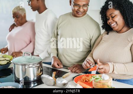 Glückliche schwarze Familienkoche in der Küche zu Hause - Tochter, Sohn, Vater und Mutter haben Spaß bei der Zubereitung vegetarischer Mittagessen - Hauptfokus auf Tochter fa Stockfoto