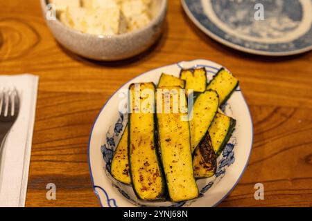 Gegrillte Zucchini-Scheiben auf dekorativer Platte mit Tofu im Hintergrund Stockfoto