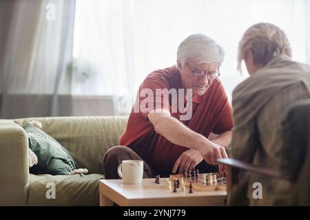 Porträt eines grauhaarigen älteren Mannes, der mit seiner Frau oder einem Freund Schach spielt und ruhige Aktivitäten in einem gemütlichen Wohnraum genießt Stockfoto