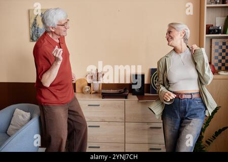 Seitliches Porträt zweier moderner Senioren, die fröhlich zusammen tanzen und Musik im Kopierraum zu Hause hören Stockfoto