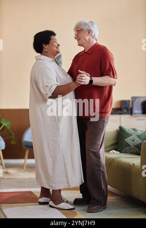 Vertikales Porträt eines multiethnischen Seniorenpaares, das zusammen tanzt und ein romantisches Date im Haus genießt Stockfoto