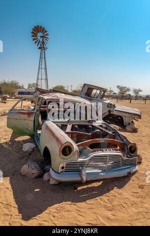 Auto- und Lastwagenwracks mit einer Windmühle in der Namib-Wüste in Solitaire, Namibia, Afrika Stockfoto