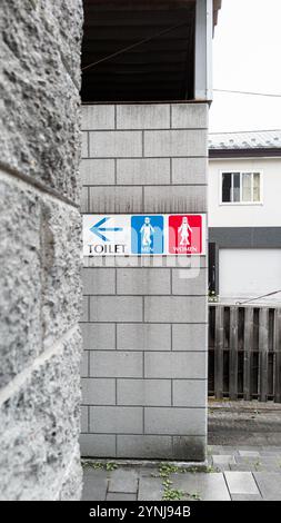 Richtungsschild für öffentliche Toiletten mit humorvollen Gender-Symbolen an der Betonmauer in urbanem Ambiente Stockfoto