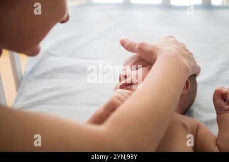 Eine Mutter wiegt ihr Neugeborenes liebevoll und berührt sanft den Kopf des Babys. Die sanfte Umgebung und das warme Licht schaffen eine ruhige Atmosphäre der Verbundenheit und Stockfoto