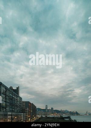 „Panoramablick auf die Skyline der urbanen Uferpromenade unter dramatischem bewölktem Himmel in der Abenddämmerung, mit Stadtlandschaft und reflektierendem Wasser“ Stockfoto