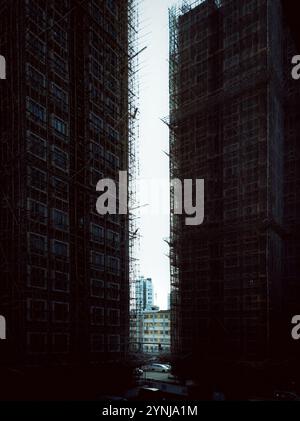 Urbanes Hochhausgebäude, eingerahmt von dunklen Gerüsten mit Blick auf die Stadtlandschaft im Hintergrund Stockfoto