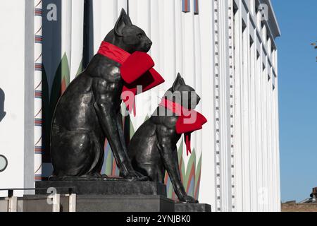 London, Großbritannien. 26. November 2024. Zwei große Katzenskulpturen, die den Eingang zum Greater London House in Mornington Crescent bewachen, sind mit festlichen roten Bögen für die Weihnachtszeit geschmückt. Das Art-Deco-Gebäude, ursprünglich die Carreras Zigarettenfabrik, ist ein Beispiel für die ägyptische Wiedergeburt-Architektur des 20. Jahrhunderts und die Katzen repräsentieren die ägyptische Göttin Bastet. Quelle: Ron Fassbender/Alamy Live News Stockfoto