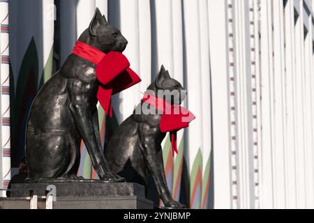 London, Großbritannien. 26. November 2024. Zwei große Katzenskulpturen, die den Eingang zum Greater London House in Mornington Crescent bewachen, sind mit festlichen roten Bögen für die Weihnachtszeit geschmückt. Das Art-Deco-Gebäude, ursprünglich die Carreras Zigarettenfabrik, ist ein Beispiel für die ägyptische Wiedergeburt-Architektur des 20. Jahrhunderts und die Katzen repräsentieren die ägyptische Göttin Bastet. Quelle: Ron Fassbender/Alamy Live News Stockfoto