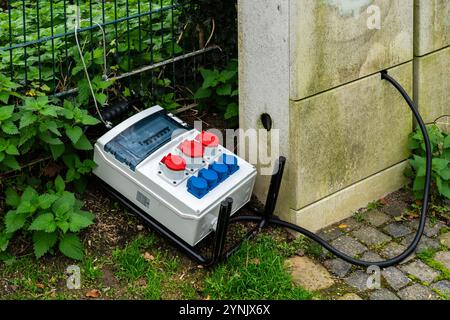 Die elektrischen Anschlüsse werden über einen Abzweigkasten hergestellt, der neben einer Wand positioniert ist und von Grün und Steinen umgeben ist, um die Außeneinrichtung zu veranschaulichen. Stockfoto