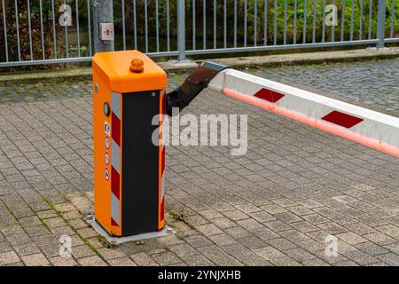 Am Eingang eines Parkplatzes befindet sich eine automatische Absperrung in Orange und Schwarz. Die Barriere ist derzeit angehoben und ermöglicht den Zugang. Stockfoto