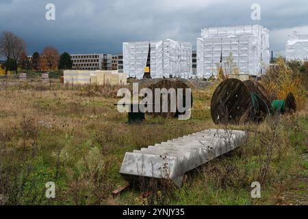 Ein verlassenes Industriegelände verfügt über bewachsenes Gras, verworfene Holzspulen und ein im Bau befindliches Gebäude, das mit weißer Polyethylenfolie bedeckt ist Stockfoto