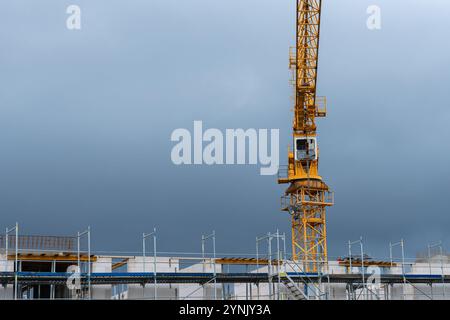 Ein gelber Kran ragt über einer aktiven Baustelle mit Gerüsten und unfertigen Bauwerken vor einem grauen, bewölkten Himmel. Stockfoto