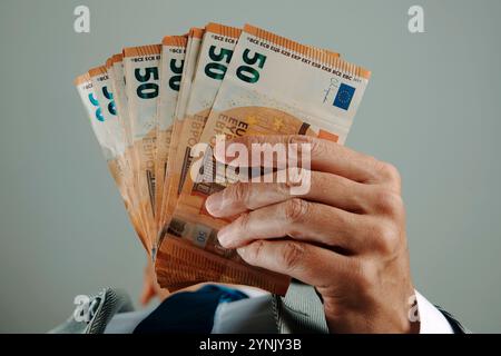 Ein Geschäftsmann trägt einen eleganten grauen Anzug, ein Hemd und eine Krawatte und hat drinnen Euro-Banknoten in der Hand Stockfoto