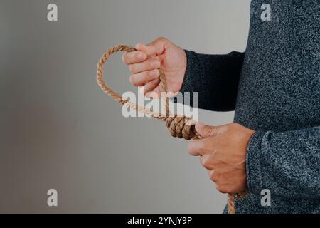 Ein Mann hält ein Jute-Seil mit einer Schlinge, auf grauem Hintergrund mit einem leeren Platz links Stockfoto