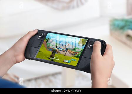 Kind, das eine Handheld-Spielkonsole hält und ein Actionspiel anzeigt. Wohnzimmer Hintergrund. Neuerungen im Bereich des Marktwachstums für Handheld-Konsolen a Stockfoto