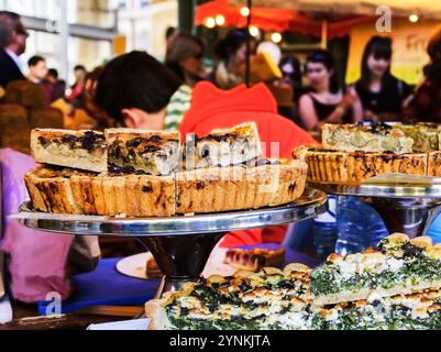 Pilze, Spinat und Brokkoli werden am Konditorstand im farbenfrohen Lebensmittelmarkt - einem berühmten Borough Market (London, England) - ausgestellt. Leute, die Foo kaufen Stockfoto