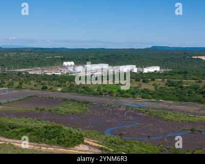 Die Luftaufnahme erfasst Industrieanlagen inmitten üppiger Grünflächen, Feuchtgebiete und ferne Berge unter hellem Himmel. Stockfoto