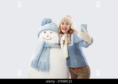 Glückliche junge Frau, die ein Selfie mit einem Schneemann macht, in warmer Strickkleidung gekleidet. Ein festlicher Skitour während der Weihnachtsferien im Sieg Stockfoto