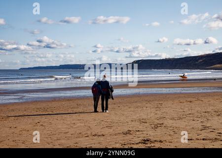 Ein Paar (Mann und Frau), das am Strand steht und die Aussicht auf die Klippen entlang der Küste am Scarborough Beach mit Blick auf das Meer, Yorkshire, England, bewundert. Stockfoto