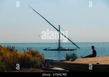 Junge sitzt auf dem Boot seines Vaters am See Stockfoto