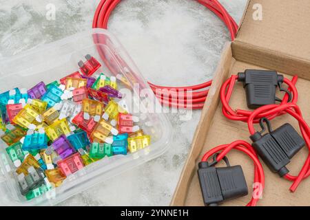 Buntes Sortiment an Kfz-Flachsicherungen und wasserdichten Sicherungshaltern auf der Tischplatte. Farbeinstufungscode für diese in Notizen. Stockfoto