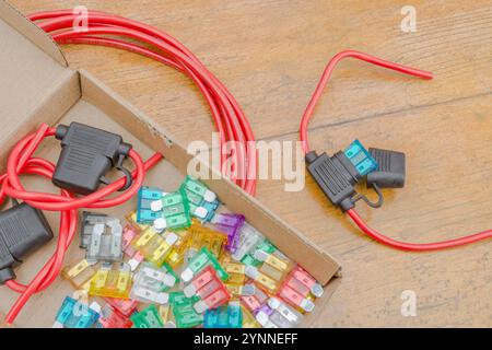 Buntes Sortiment an Kfz-Flachsicherungen und wasserdichten Sicherungshaltern auf der Tischplatte. Farbeinstufungscode für diese in Notizen. Stockfoto