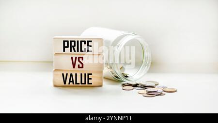 Holzblöcke mit der Aufschrift „Price Against Value“ auf weißem Hintergrund mit einem Glas mit Pfennigen Stockfoto