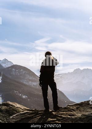 Ein einsamer Wanderer steht auf einer felsigen Klippe und bestaunt nebelnde Berggipfel unter einem riesigen Himmel. Inspiriert von der Romantik ruft die Szene Introspektion und Sp Stockfoto