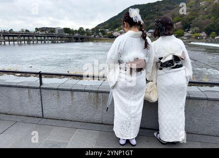 Zwei junge Frauen in traditioneller japanischer Kleidung mit Blick auf den Uji-Fluss und die Brücke, Rückansicht. Kirschblütensaison in Kyoto, Japan. Stockfoto