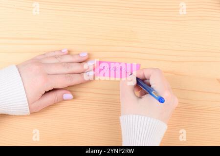 Junge Frau schreibt Danke Note mit blauem Stift auf hölzernem Hintergrund. Kopierbereich. Stockfoto