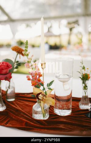 Elegante Einrichtung im Hinterhof mit farbenfrohen Herbstblumen, Messing-Kerzenleuchtern und einer Tischläufer aus Terrakotta-Samt. Stockfoto