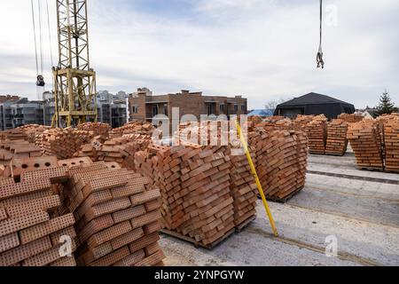 Stapel von roten Ziegeln auf einer Baustelle mit einem Kran und unfertigen Gebäuden im Hintergrund Stockfoto