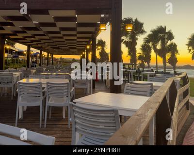 Abendessen bei Sonnenuntergang in einem Restaurant am Strand mit leeren Tischen und Palmen im Blick Stockfoto