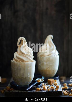 Zwei Eisbecher gefüllt mit Karamell-Weicheis, auf dunklem hölzernem Hintergrund Stockfoto