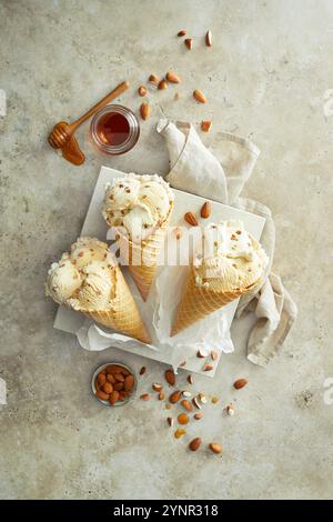 Mandel-Honig-Eis in drei knusprigen Eiskegeln zubereitet, auf einem weißen Teller angeordnet, dekoriert mit Mandeln und Honig auf einem beigen Stein Backgrou Stockfoto