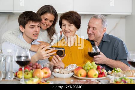 Glückliche Familienmitglieder, die auf den Bildschirm des Mobiltelefons schauen, über Videos oder Fotos in sozialen Netzwerken lachen, Spaß zu Hause haben Stockfoto