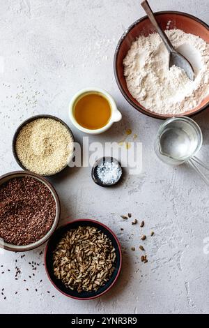 Eine Auswahl an Kochzutaten einschließlich Mehl, Sesamsamen, Leinsamen, Sonnenblumenkernen, Öl, und Salz auf einer strukturierten Oberfläche angeordnet. Stockfoto
