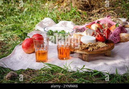 Picknickszene mit Blick auf das Leben mit frischen Granatäpfeln, Walnüssen, Pinienkernen und cremigem Weißkäse auf einem Holzbrett, natürlichem Sonnenlicht-Pomegra Stockfoto