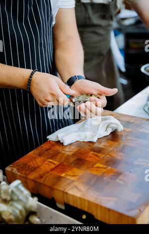 Der Koch öffnet frische Austern auf einem Holzbrett für eine Platte mit Meeresfrüchten und betont die kulinarische Präzision Stockfoto