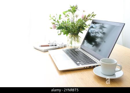 Heller, femininer Arbeitsbereich mit Laptop, Kaffee und Blumen auf einem Holztisch in einem gemütlichen Home Office, Hintergrund verblasst in weiß, Konzept für Business, St. Stockfoto