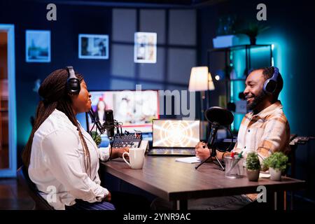 Fröhliche afroamerikanische Content-Ersteller, die Podcasts produzieren und Live-Chats für Online-Hörer bereitstellen. Schwarze Männer und Frauen, die ihre Talkshow über Aufnahmegeräte übertragen. Stockfoto