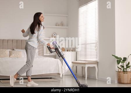 Junge Frau, die den Boden mit schnurlosem Staubsauger im Schlafzimmer reinigt Stockfoto