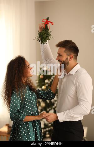 Ein reizendes Paar unter Mistelzweigen im Zimmer, das zu Weihnachten dekoriert war Stockfoto