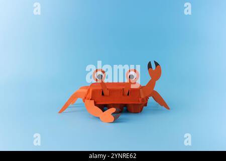 Handgemachte Krabbenhandwerk aus bemaltem orangenem Eierkarton mit Papierklauen und Augen auf blauem Hintergrund. Studio-Fotografie. Sommerkreation und Stockfoto