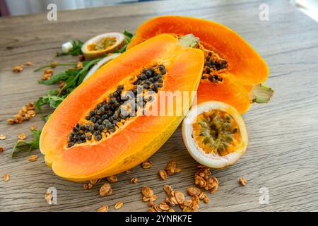 Papaya-Frucht, Passionsfrucht, Rucola und Müsli auf hellem hölzernem Hintergrund. Scheiben süßer Papaya, Maracuja, grüner Rucola umgeben von Granola fla Stockfoto