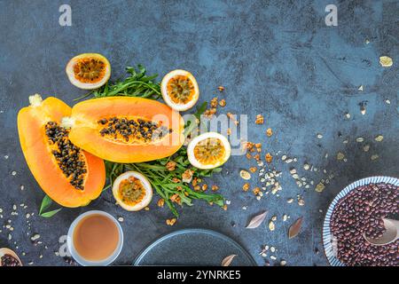 Papaya, Passionsfrucht, Rucola und Müsli auf einem blauen Stein Küchentisch Hintergrund. Scheiben süßer Papaya, Passionsfrucht und Rucola umgeben von Gra Stockfoto