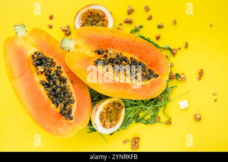 Papaya, Passionsfrucht, Rucola und Müsli auf gelbem Hintergrund. Scheiben von süßer Papaya, Passionsfrucht, Rucola umgeben von Granola Flocken auf Gelb Stockfoto